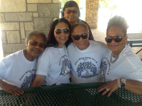 Friends gather at a park wearing matching shirts, enjoying their time together with laughter.