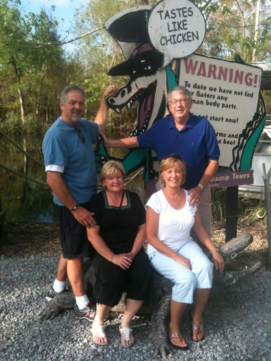 Four friends pose playfully by a large warning sign at a scenic outdoor location during summer.