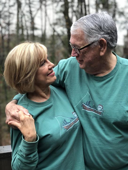 A couple smiles affectionately in a peaceful, tree-filled outdoor setting.