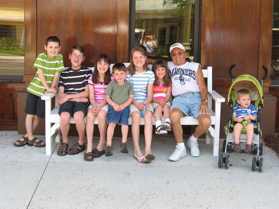 A happy group of kids poses on a bench outside on a sunny day, enjoying time together.