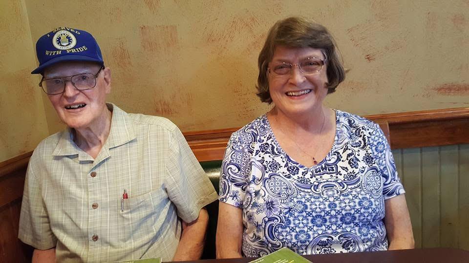 Elderly man and woman smile warmly while enjoying lunch at a cozy restaurant together.