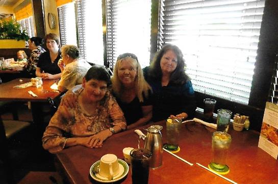Three friends share laughter and drinks while enjoying a lively brunch atmosphere at a cafe.