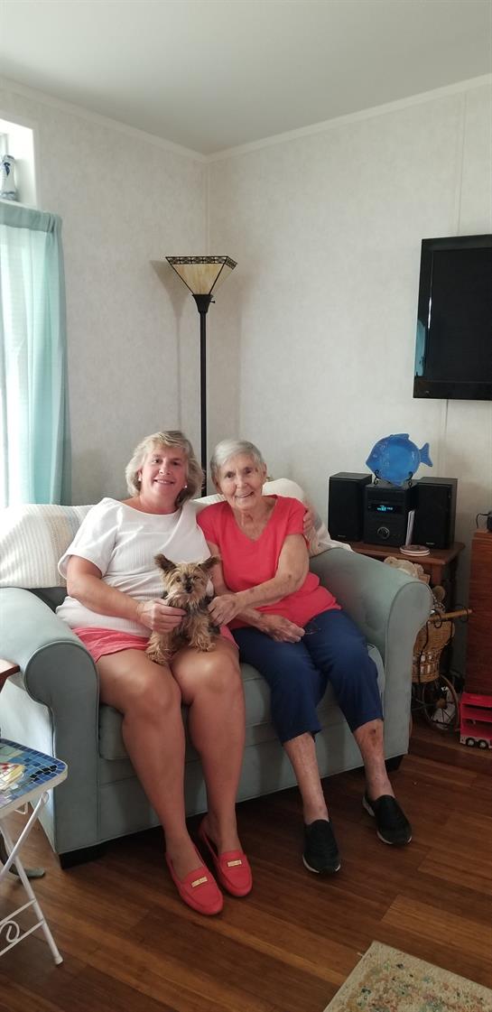 Two women sit together on a couch, holding a small dog in a warm and inviting living room.