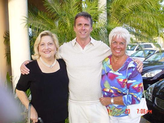 Portrait of three friends smiling and posing together outdoors on a warm day surrounded by greenery.