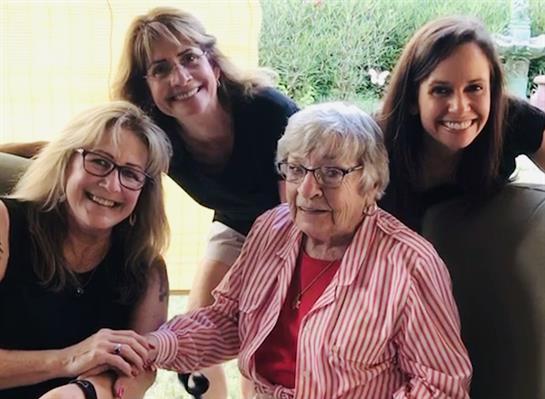 Four women smile joyfully while posing for a photo together outdoors, showcasing their bond.
