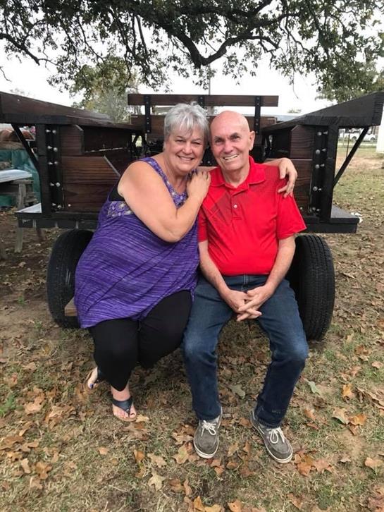 Two people share a joyful moment outdoors, seated comfortably beside a wooden trailer in the park.