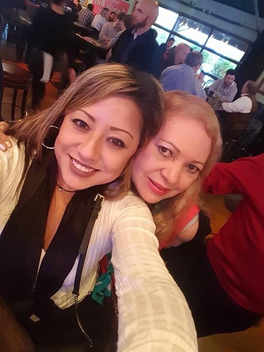 Two friends smile while taking a selfie at a vibrant restaurant filled with people.