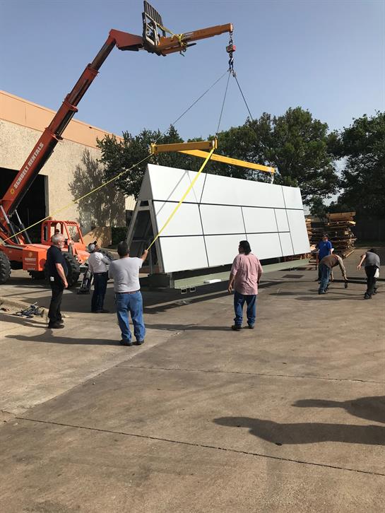 Crew members coordinate to lift a massive panel using a crane at a construction site.