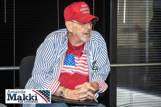 An older man in red, white, and blue shares political views at a local event.