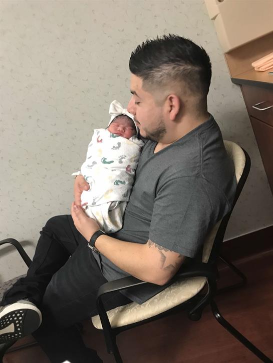 Father enjoys special time holding his swaddled newborn in a cozy hospital setting.