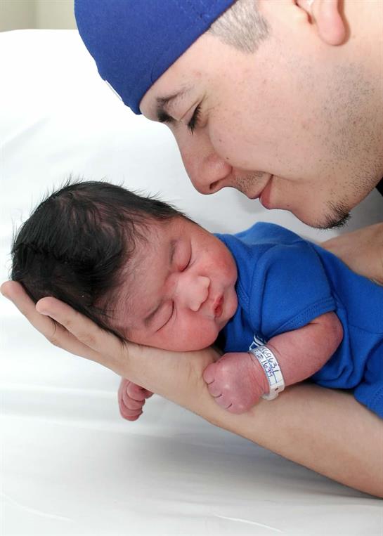 A father gently holds his newborn baby, sharing a sweet moment in a hospital setting.