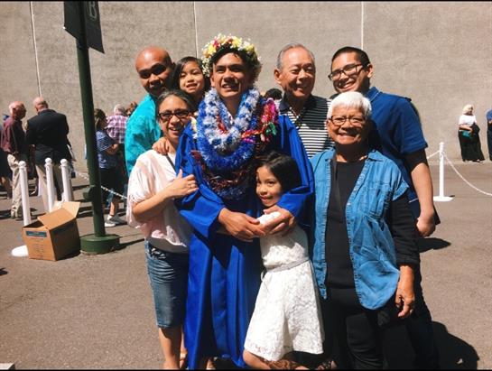 A proud graduate poses with family members in a cheerful outdoor gathering, celebrating success.