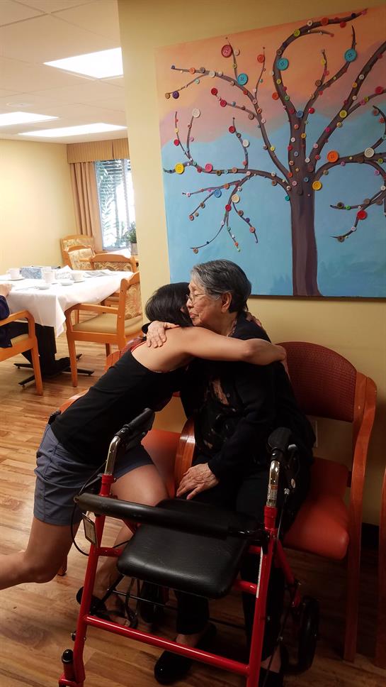 A young woman hugs her grandmother in a care home, capturing a heartfelt family moment.