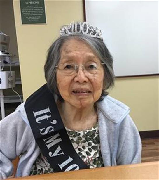 A woman in a tiara and sash celebrates her 100th birthday surrounded by joy and warmth.