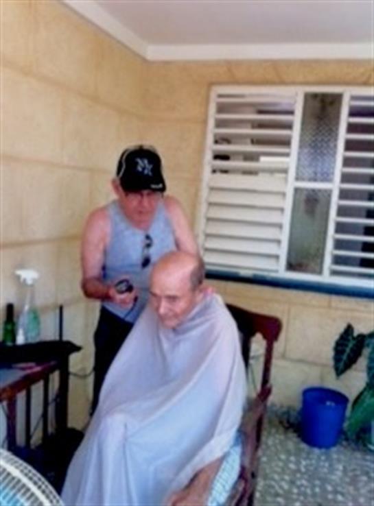 A skilled barber cuts the hair of an elderly man on a warm day, showcasing a relaxed atmosphere.