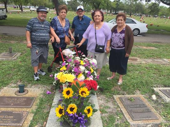 Five family members stand together, honoring a loved one with colorful flowers at a gravesite.