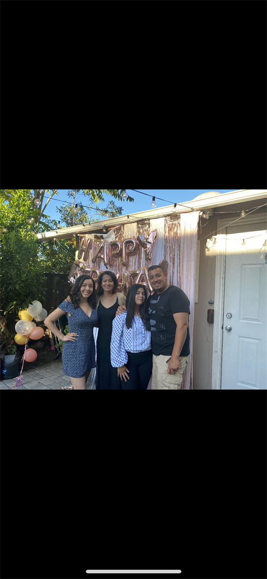 Family members pose together at a joyful celebration with decorations and balloons in a backyard.