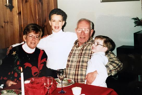 Four family members smile happily while enjoying a meal together in a warm indoor setting.