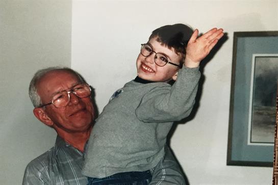 Grandfather lifts his happy grandson in glasses, both enjoying a warm atmosphere.