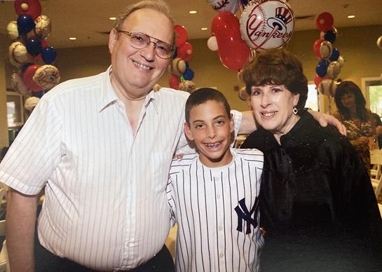 Three family members pose happily together at a festive gathering decorated with balloons.