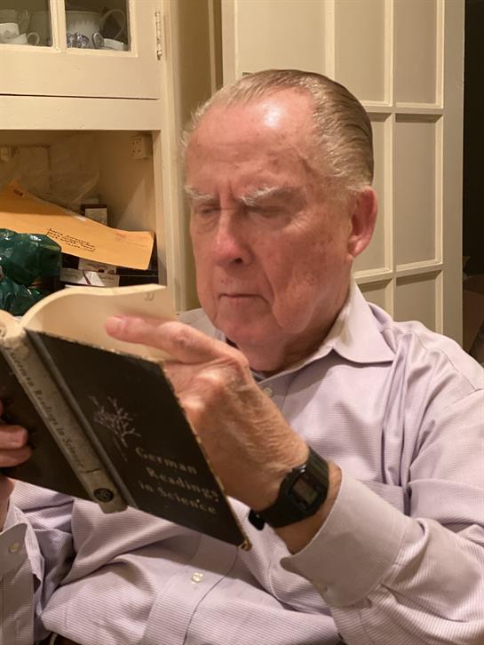 An elderly man concentrates on reading a book in a warm, inviting indoor space during the evening.