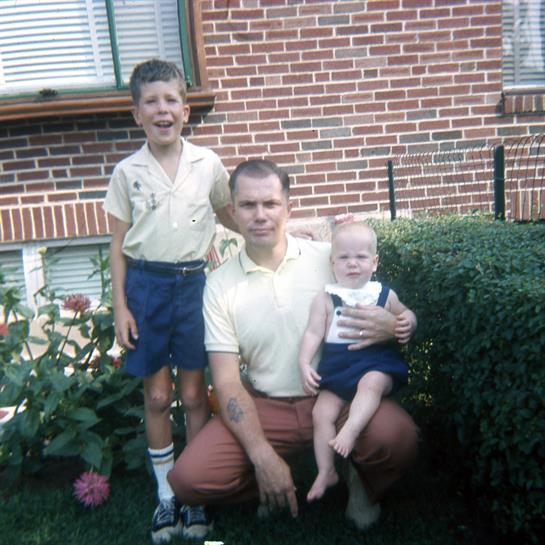 A father poses with his two children in a green backyard, sharing a joyful moment during summer.