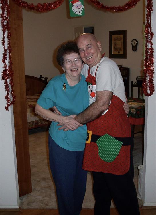 Joyful couple shares a dance in holiday attire, surrounded by decorations and warmth of home.