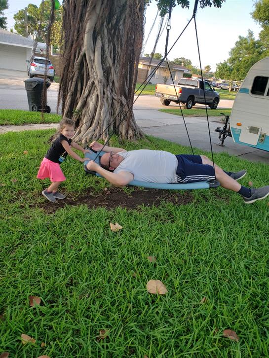 A little girl joyfully pulls her grandfather on a swing while they relax outdoors.