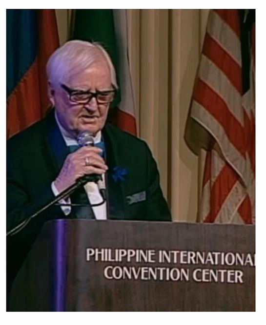 A speaker shares insights at a formal event taking place in Manila, with flags in the background.