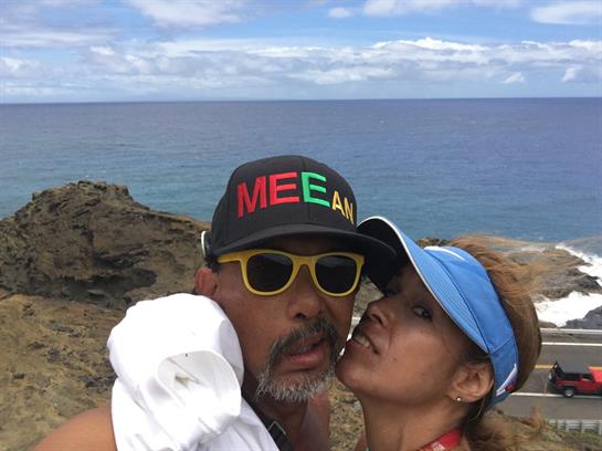 A couple smiles for selfies with the ocean and sky in the background, enjoying their time together.