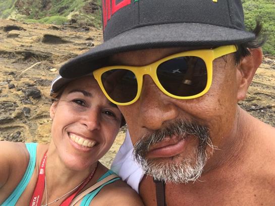 Two friends smile broadly while taking a selfie during a sunny beach outing.