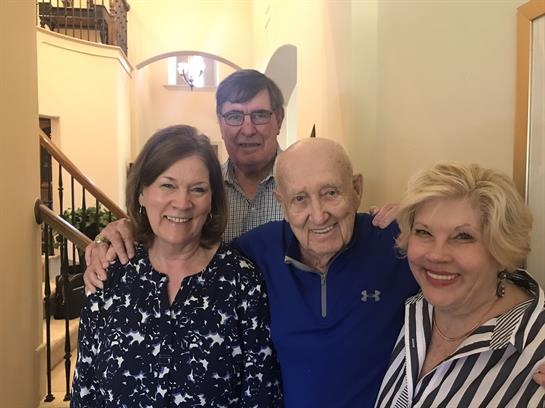 A cheerful family shares a moment with an elderly man in a home setting during the afternoon.