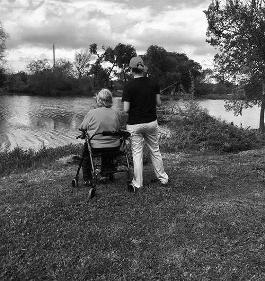 An elderly woman enjoys the serene lakeside view with her caregiver on a sunny afternoon.