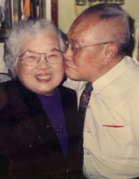 An elderly couple smiles warmly as they embrace at a joyful family gathering.