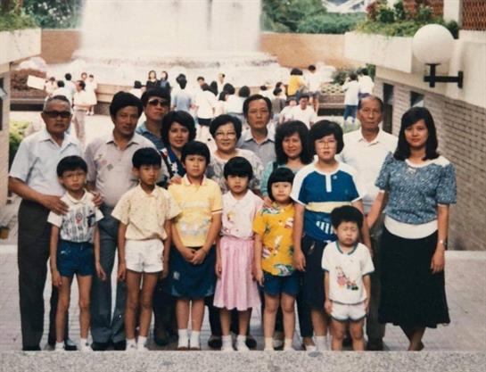 A large group of family members gathers together in a park setting, smiling and posing.