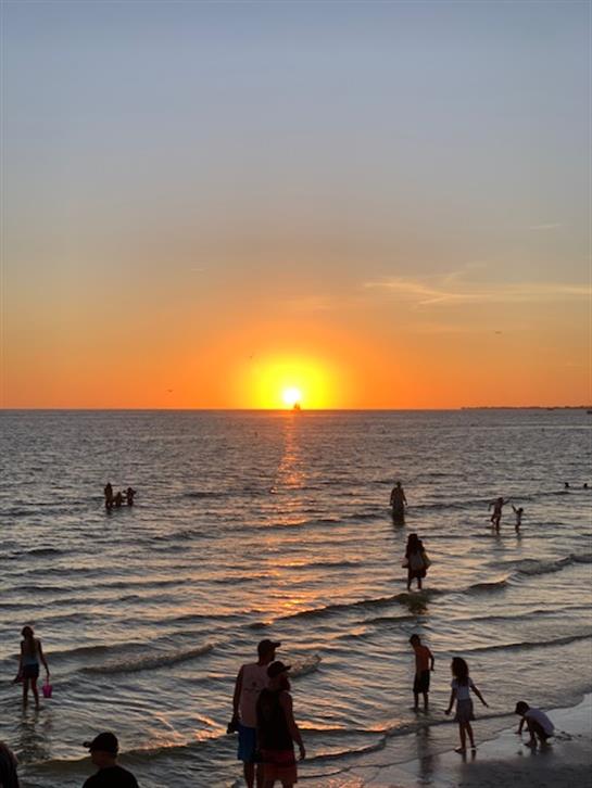 Warm sunset casts vibrant colors on the ocean as beachgoers wade in the gentle waves.