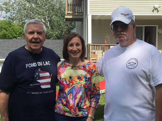 Three people stand together in a backyard enjoying a sunny day filled with laughter and joy.