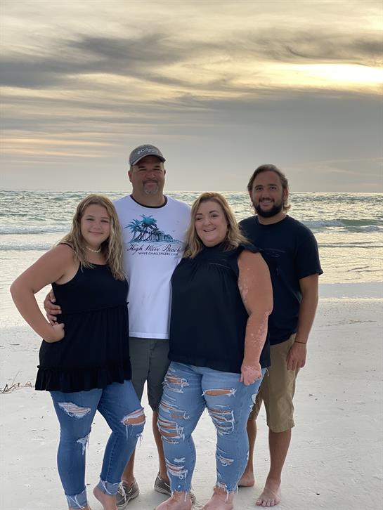Four family members gather on the beach during sunset, smiling happily as they pose together.