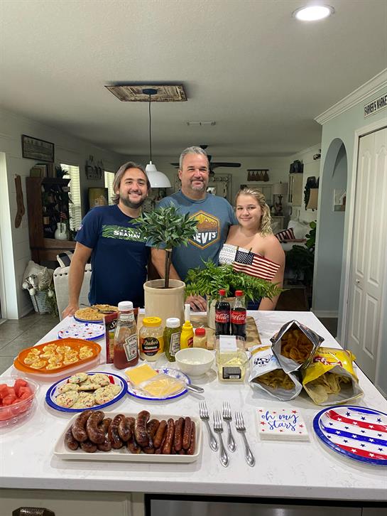 Family members gather around a table filled with festive food items, celebrating together in summer.