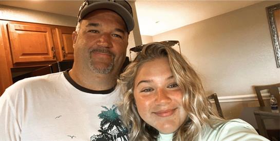 Father and daughter share a joyful moment indoors, both smiling widely at the camera.
