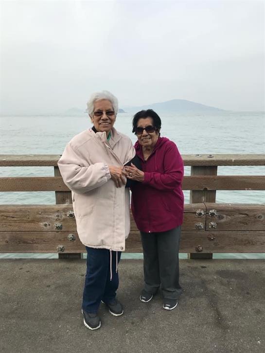 Elderly women smile and bond together on a wooden pier by the water.