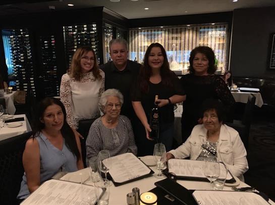 Seven individuals pose together in a beautifully arranged restaurant, celebrating over dinner.
