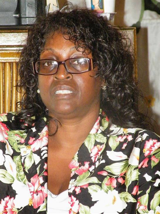 A woman with curly hair wearing a floral top expresses contemplation while sitting indoors.