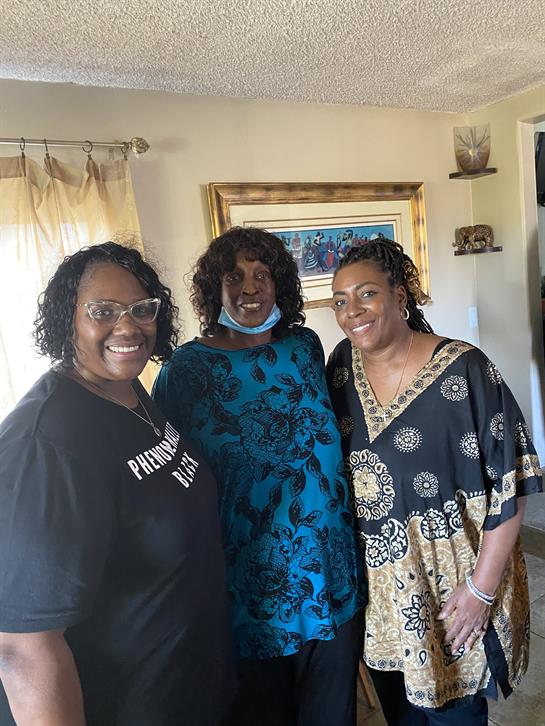 Three women smile joyfully together in a bright living room, celebrating a special moment.