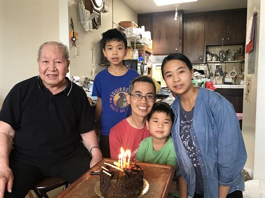 A joyful family gathers around a birthday cake with candles in a warm, inviting kitchen.