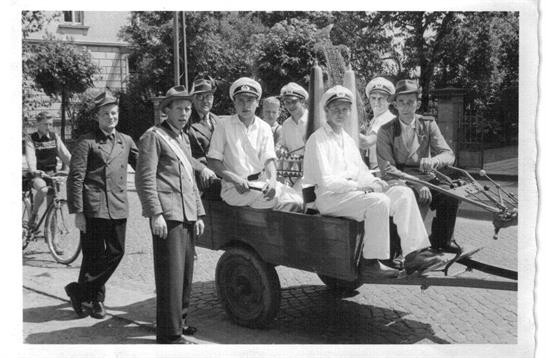 A diverse group gathers around a cart, smiling in a daytime historical village.