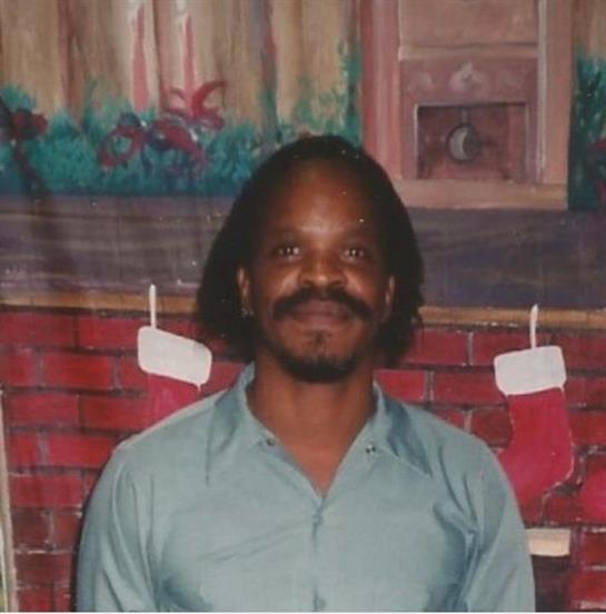 Man smiles broadly in a cozy room adorned with holiday decorations and stockings.