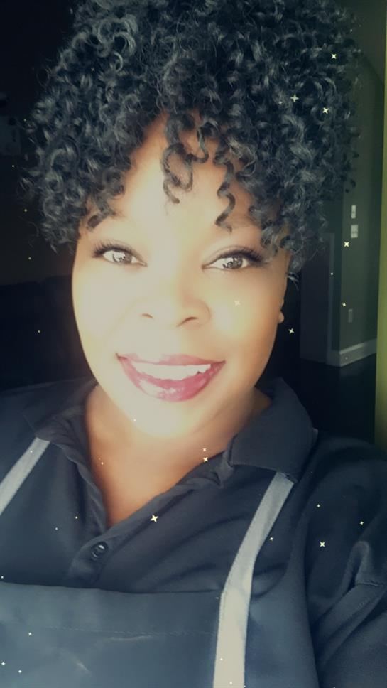 A joyful woman with curly hair smiles warmly in natural light.