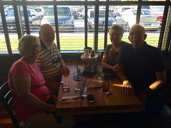 Four elderly friends sit around a table, enjoying drinks and engaging in lively conversation.