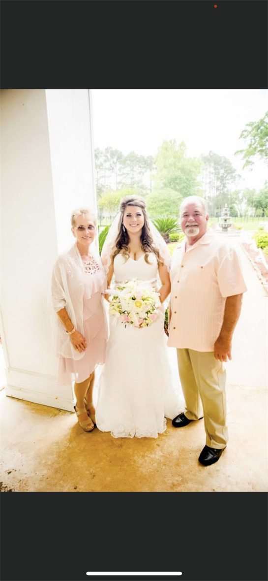 Joyful couple poses with their daughter in a lush garden, celebrating a beautiful wedding moment.